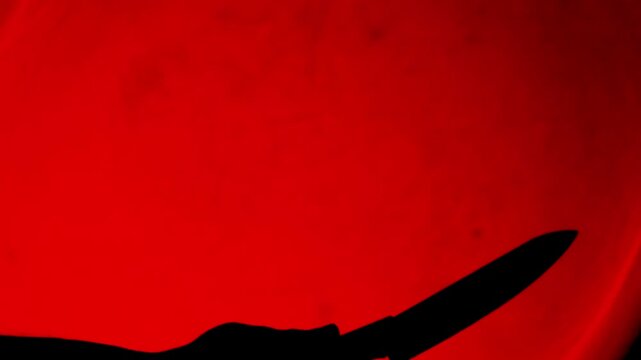 Silhouette man holding knife in red light. The shadow of a murderer kills his victim with a knife at night.