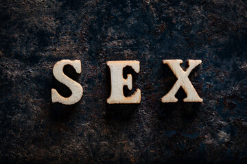 Wooden letters with the word sex on an old rusty surface, closeup, top view. The concept of sex question, sexual health, sex education