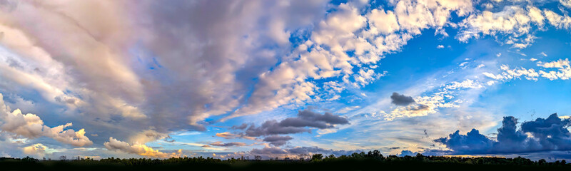 Sunset with sun and clouds on blue and orange dramatic sky with sun rays. A stroll along the forest shape silhouettes. Ultrawide color and light evening golden hours endless space and tranquility