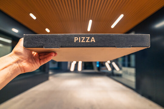 Hand holding pizza box outdoors in urban setting