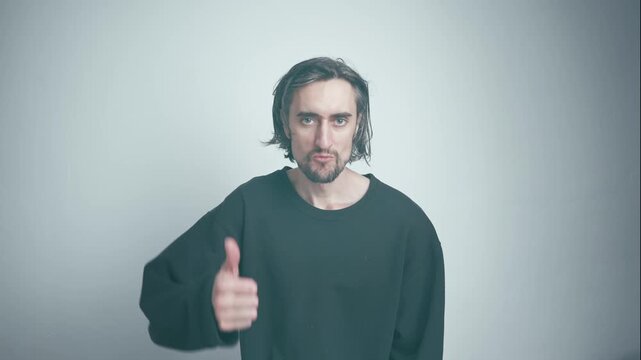 Like, Cool, Thumbs Up: Middle-aged man with long greying hair in oversized black sweatshirt shifts from calm demeanor to a smirk and thumbs up against a softly-lit background.