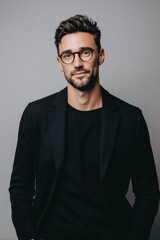 Obraz premium A confident young man with glasses dressed in a black blazer and black shirt.