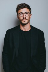 Obraz premium A confident young man with glasses dressed in a black blazer and black shirt.