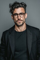 Obraz premium A confident young man with glasses dressed in a black blazer and black shirt.