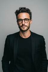Fototapeta premium A confident young man with glasses dressed in a black blazer and black shirt.