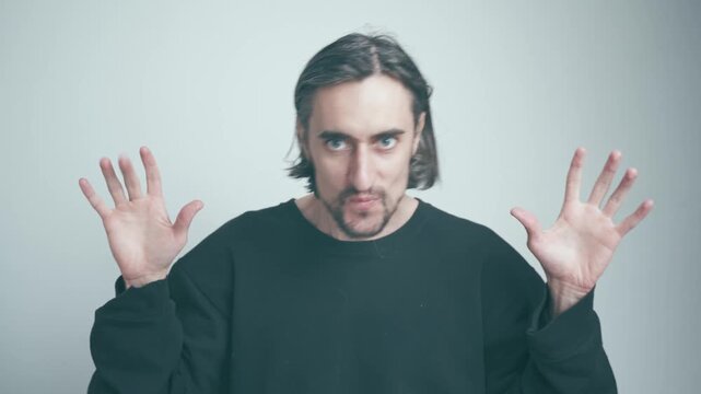 Sly Smile and Cringy Dance: Man in Black Sweatshirt Engagingly Emphasizes Key Points with Hand Gestures Against a Light Background