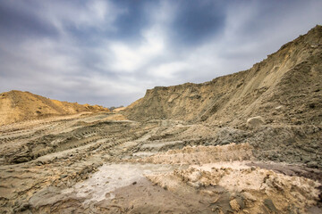Heavy machinery has moved large amounts of earth, creating mounds and deep tracks at a construction site under a cloudy sky in the afternoon