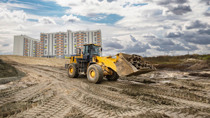 Obraz premium Heavy machinery is seen moving earth at a construction site close to new apartment buildings on an overcast day, preparing the land for future development