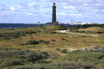 Landscape photo with a view of the Skagen Gray Lighthouse and green hills in the foreground at Cape Grenen, in Skagen, northern Denmark