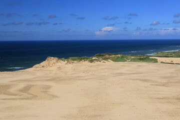 Landscape photo with a view of the North Sea and sand dunes against a blue sky with clouds near the Rubjerg Knude lighthouse in Denmark