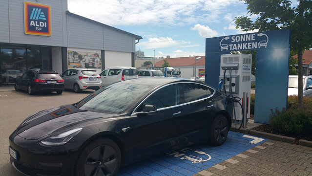Memmingen, Germany - June 30, 2020:  A static shot of a solid black Tesla Model 3 dual motor long range awd charging at the Aldi DC charging station in a cloudy summer day.