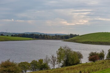 A wide shot of a loch surrounded by rolling green hills under a cloudy sky in Killington Lake - Kendal - Lake District - UK