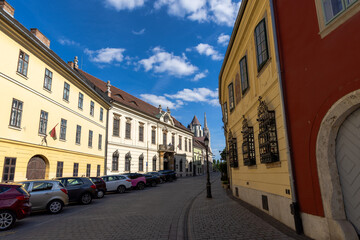 Obraz premium Picturesque European street with colorful historic buildings, parked cars, and bright blue sky with clouds, capturing the charm of old town architecture.