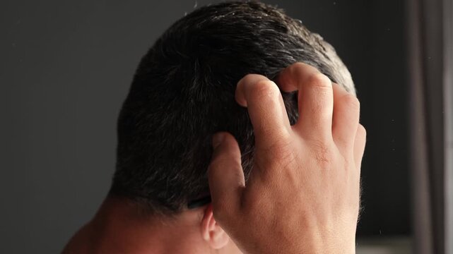 A man with short gray hair scratches his whole head