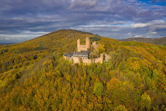 Aerial view of the stark stone Auerbach Castle atop a hill ablaze with autumnal colors under a dramatic sky, Bensheim, Hessen, Germany.