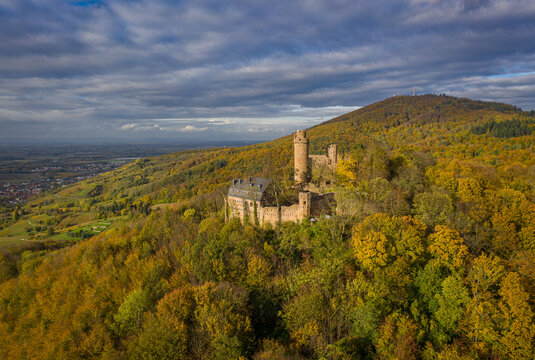 Aerial view of Auerbach castle perched atop a hill, surrounded by a forest painted in autumn hues under a dramatic sky, Bensheim, Hessen, Germany.