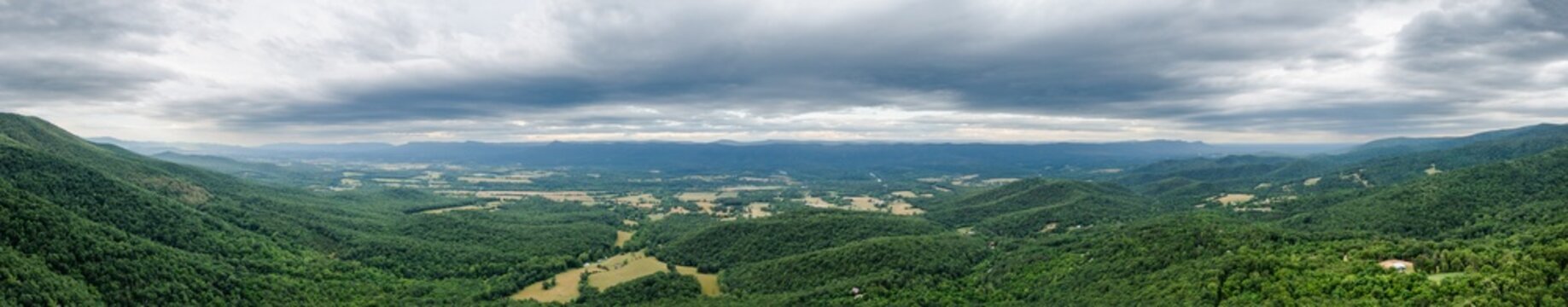 Aerial view of rolling green hills meeting the horizon under a stormy sky, with fields of gold and lush forests creating a rich tapestry, Rileyville, Virginia, USA.