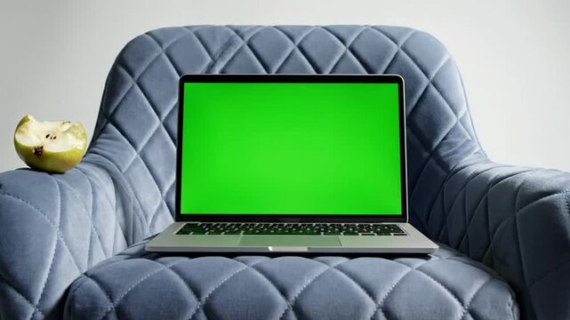Laptop with green screen on blue armchair with apple core.