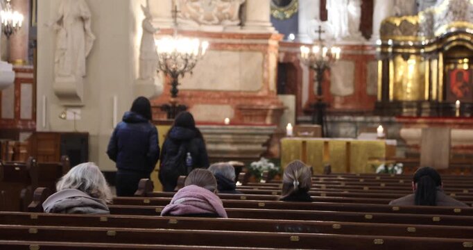 Worshippers sit scattered across wooden pews during a quiet service in a Baroque church; warm chandeliers and altar candles glow softly, evoking contemplation, faith, and calm.