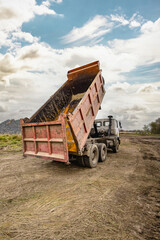 Obraz premium A dump truck is unloading a load of dirt at a construction site surrounded by a rural landscape. It is an overcast day with visible clouds