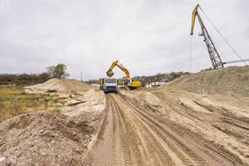 Heavy machinery like dump trucks and excavators operate in a construction area, moving earth and...