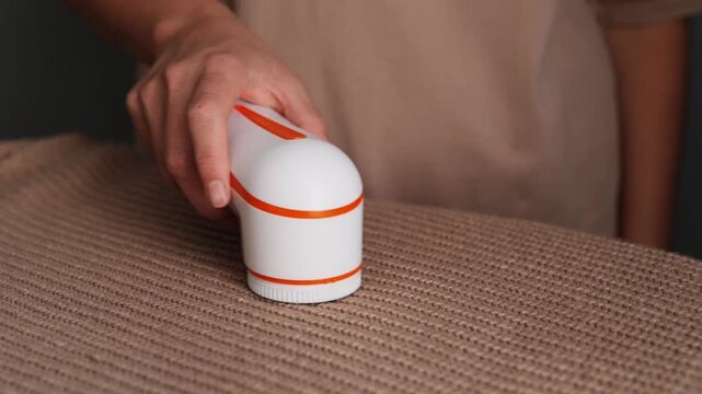 A person uses a handheld lint remover on a textured fabric at home to easily remove lint and dust, keeping clothing looking fresh and neat