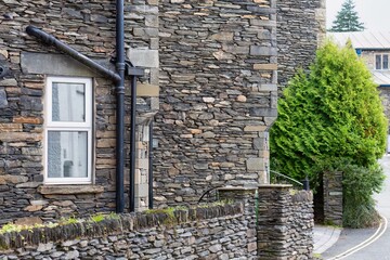 A picturesque stone building with a white-framed window, set against a textured stone wall in Bowness-on-Windermere - Lake District - UK