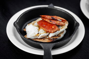 Grilled fish fillet with chorizo slices in pan