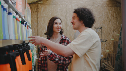 Two friends share smiles while exploring a vibrant greenhouse filled with various gardening tools...