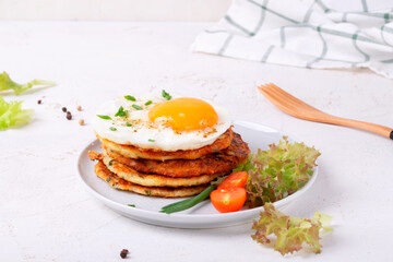 Fried egg on the stack of zucchini fritters with fresh vegetables. Served breakfast on the plate