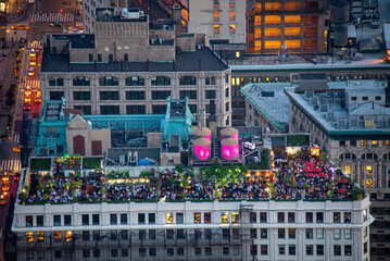 View of a rooftop terrace bustling with people under soft pink lights, contrasting with the city's warm glow, a vibrant scene, New York, New York, United States.