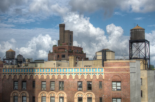 View of brick buildings adorned with intricate blue and gold patterns, topped with water towers against a backdrop of fluffy clouds, New York, New York, United States.