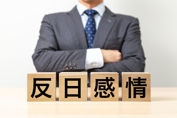 「反日感情」と書かれたブロックと腕組みをするビジネスマン