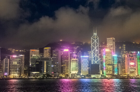 View of vibrant skyscrapers, glittering like jewels against the dark sky, reflect in the still waters of Hong Kong's harbor, Hong Kong, China.