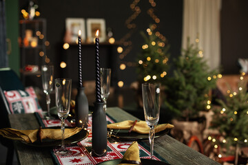 Holiday dinner table with black spiral candles, champagne flutes, gold napkins, and a redwhite...
