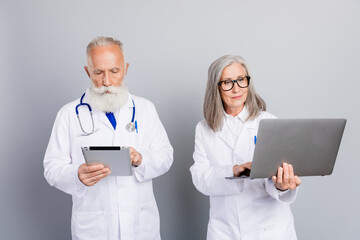 Two experienced doctors review patient information using tablet and laptop in a modern clinic setting