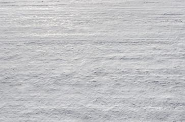 A textured, snow-covered surface showing subtle drifts and horizontal lines created by wind or...