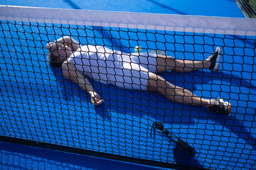 Woman in sportswear lying exhausted on a padel court after the game