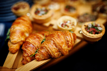 Fresh croissants and mini tarts on wooden tray