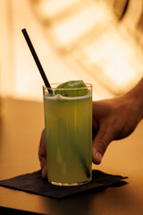 Hand holding green cocktail with straw and basil leaf