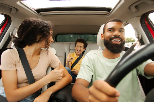 Excited African American parents and son enjoying car journey, mother looking at her son and showing thumbs up, father driving auto with smile - Powered by Adobe