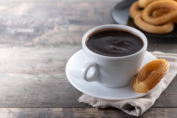 Spanish churros with hot thick chocolate in a white cup on wooden table. Copy space
