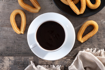 Spanish churros with hot thick chocolate in a white cup on wooden table