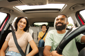Happy Latin parents looking at son through rearview mirror, man riding car, family enjoying road...