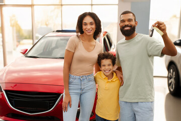 Excited black family showing new car key, standing near auto outdoor, parents and their preteen son...
