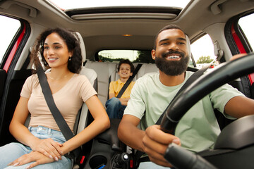 Obraz premium Road trip. Happy Black family of three riding car and smiling, traveling by automobile. Latin parents and son enjoying auto ride together