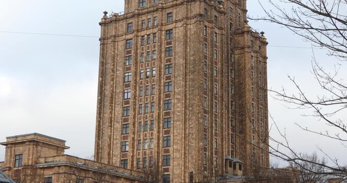 Close-up of the Latvian Academy of Sciences, a Soviet-era Stalinist tower rising against bright clouds in Riga. Ornate tiers and a sharp spire show monumental socialist classicism and layered history.
