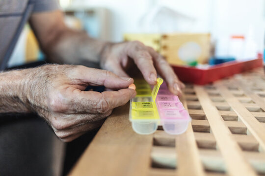 Elderly person, hand and pill box for daily medication, health and prescription medicine, sick and old age. Vitamins, supplements and senior with pills for the week, healthcare and retirement.