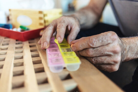 Pills, container and hands with medicine, table and healthcare for elderly person, medical and home. House, pharmaceutical and healthy for old man, closeup and storage for supplement of treatment.
