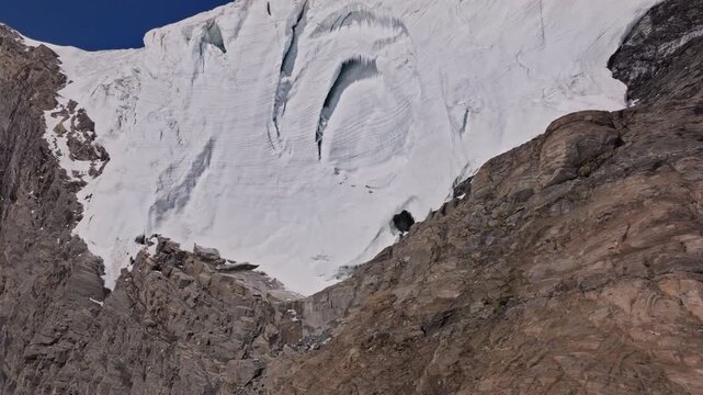 A powerful drone shot revealing massive overhanging seracs and towering ice cliffs in Saas-Fee, Switzerland. The frozen formations glisten under alpine light, showcasing the raw power of the glacier.